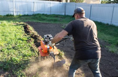 Tarlada çalışan bir adam, iş kıyafetleriyle motor bloğunu damlatan bir adam.