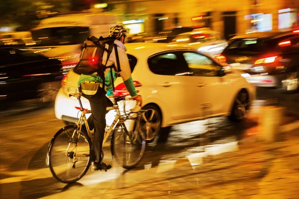 Bicycle messenger in city traffic at night — Stock Photo, Image