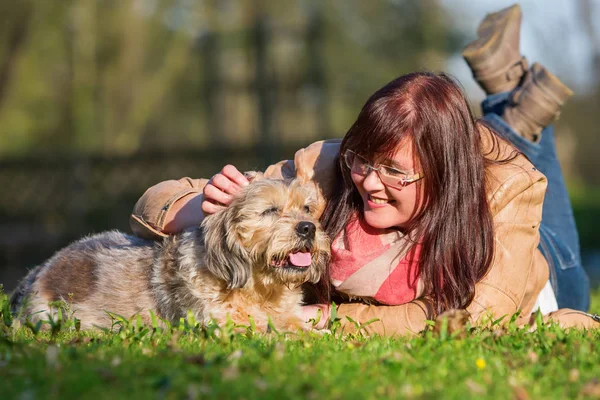 Jovem mulher encontra-se com seu cão na grama — Fotografia de Stock