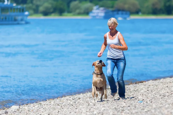 Зрелая женщина бегает с собакой на берегу реки — стоковое фото