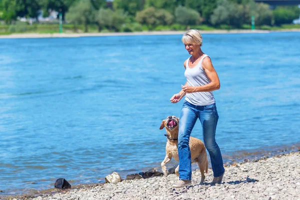 Reife Frau joggt mit Hund am Flussufer — Stockfoto