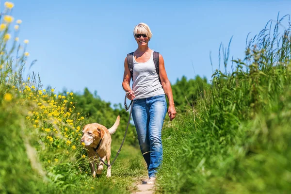 Reife Frau mit Hund beim Wandern auf dem Land — Stockfoto