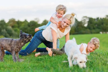 woman romps with her two sons and two dogs on the grass clipart