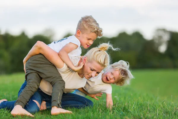 Mujer retoza con sus dos hijos en la hierba — Foto de Stock