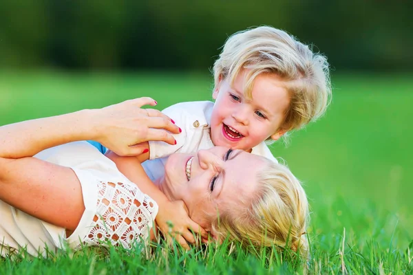 Woman romps with her son on the grass Stock Image