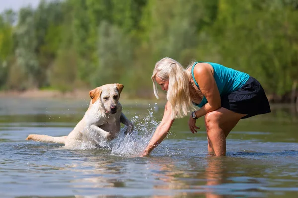 Wanita cantik bermain dengan anjing labrador di danau — Stok Foto