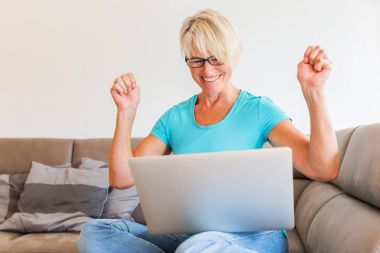 mature woman sits rejoicing in front of a laptop clipart