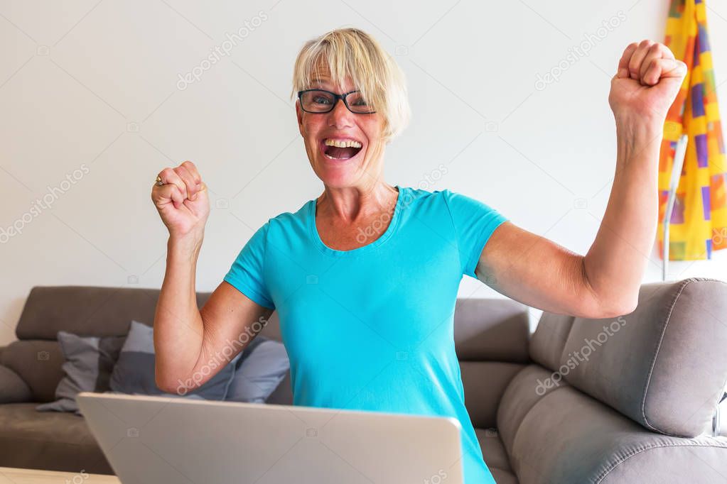 mature woman sits rejoicing in front of a laptop