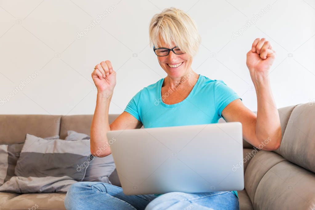 mature woman sits rejoicing in front of a laptop