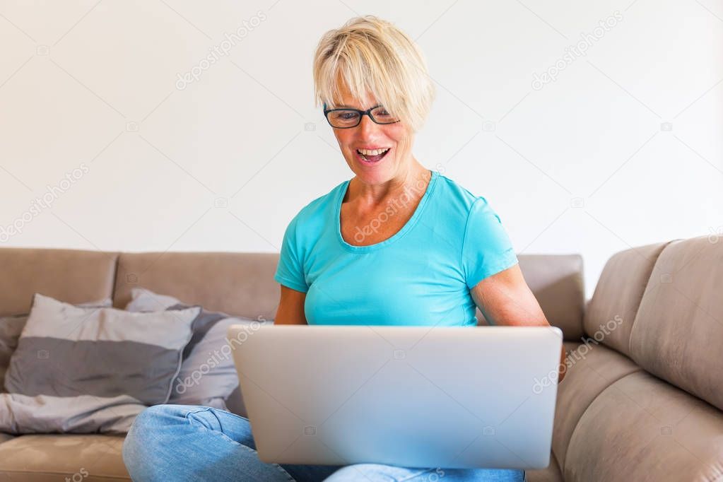 mature woman sits who is rejoicing with raised hands in front of a laptop