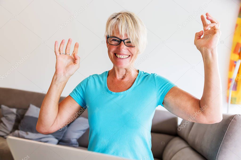 mature woman sits who is rejoicing with raised hands in front of a laptop