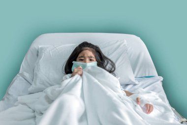 Maskeli hasta Asyalı çocuk hastane yatağında doktor muayenehanesiyle yatıyor.