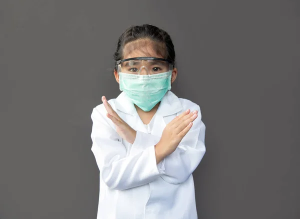 asian kids with protect mask and protect glass show open hand as stop action with doctor costume on dark background