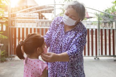 Büyük ebeveyn, evden çıkmadan önce Corona virüsünü korumak için çocuklara yüz maskesi takıyor.