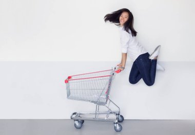 Mutlu Asyalı kadın beyaz arka planda alışveriş arabasıyla alışveriş yapmaya bayılır..