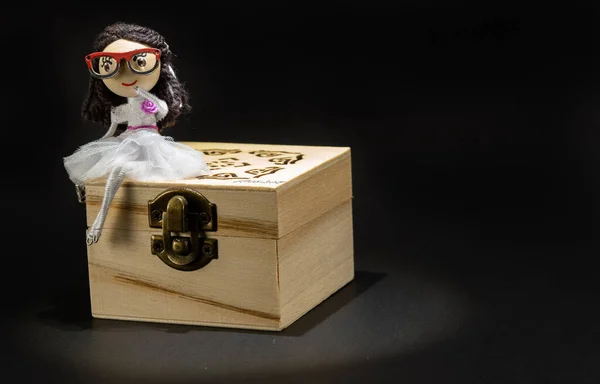 Tahta bir hazine sandığının üzerinde oturan oyuncak bebek. Kız hazine sandığını koruyor.