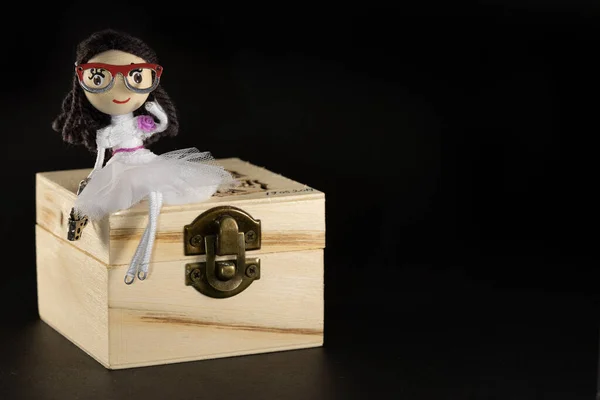 Tahta bir hazine sandığının üzerinde oturan oyuncak bebek. Kız hazine sandığını koruyor.