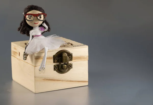 Tahta bir hazine sandığının üzerinde oturan oyuncak bebek. Kız hazine sandığını koruyor.