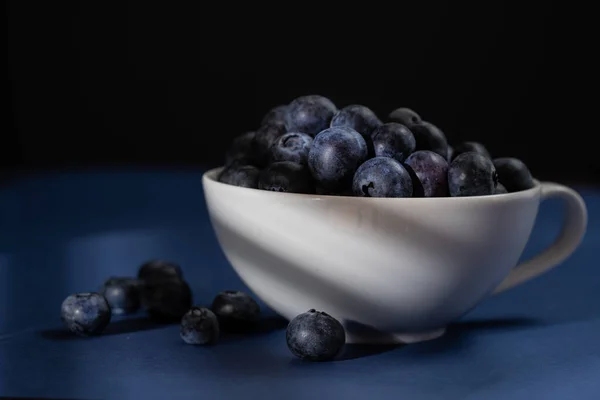 Karanlık ve kasvetli ışıkta bir fincan taze yaban mersini. Koyu mavi arkaplan