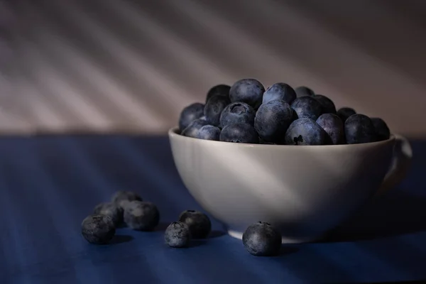 Karanlık ve kasvetli ışıkta bir fincan taze yaban mersini. Koyu mavi arkaplan