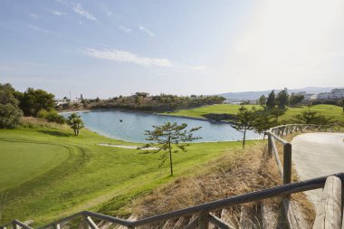 Mavi gökyüzü olan güzel bir manzara ve çimlerin üzerinde köprüsü ve gölü olan golf kulübünde güzel bir yeşil.