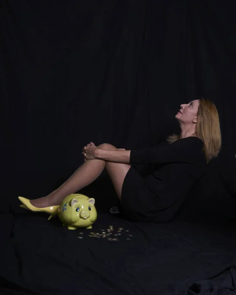 貯金の貯金を手に貯金の貯金箱を観察する実業家黒いスーツと黄色のハイヒールを持つ実業家 — ストック写真