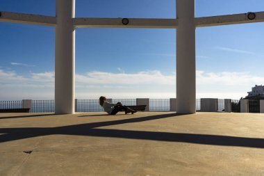 Güzel bir kadın. Arkasında deniz olan 50 yaşında, yerde oturuyor.