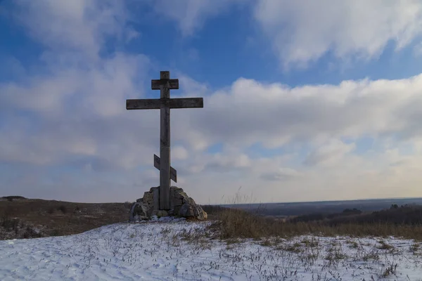 religious wooden cross on a snowy hill   against the blue sky. winter in the countryside