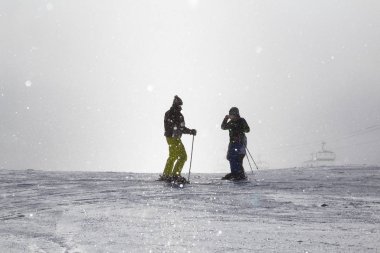 İki kayakçı puslu kayak yamacında fotoğraf çekiyor. .