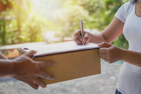 Kadın teslimat personelinin paket makbuzunu onaylamak için verdiği belgeleri imzalıyor.