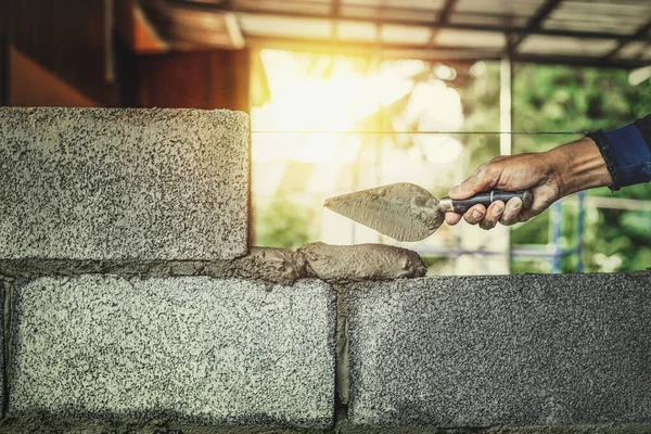 Construction workers are building cement walls with brick blocks.