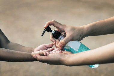 Genç kadınlar çocukların mikroplarını temizlemek için el dezenfektanı kullanırlar..