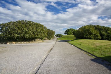 Mavi gökyüzü, bulutlar ve güneş ışığı ile bir park fotoğrafı