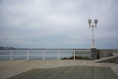 Soğuk renkleri olan manzara, bulutlu gökyüzü ve metal parmaklıklar.