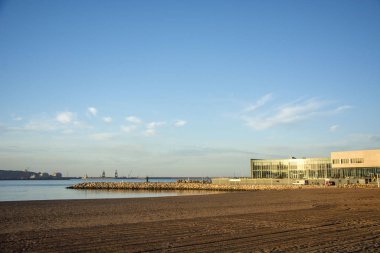 Bulutlu gökyüzü, kum ve güneş ışığı olan bir plajın fotoğrafı.