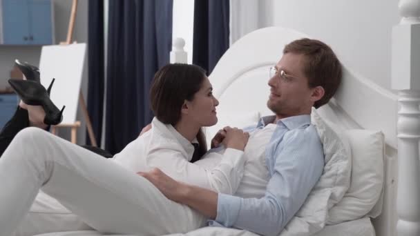 Una chica con camisa blanca habla con su marido en la cama — Vídeo de stock