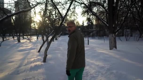Vousatý muž běží na zasněžené stopě přes městskou zahradu — Stock video