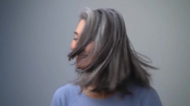 Güzel görünümlü orta yaşlı kadın, gri arka planda model olarak rol yapıyor. Onu bir yandan bir yana salladı ve doğruca kameraya baktı. Yavaş Hareket