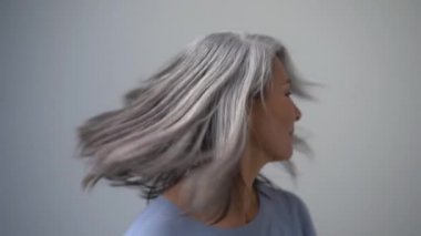 Gri saçlı, güzel Asyalı kadın saçlarını sallıyor ve gülümsüyor. Yüzü kırışıklıklarla kaplı. Mutlu Kadın. Yavaş Hareket