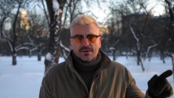 Handsom Hipster dans les lunettes de soleil jaunes debout dans le parc enneigé ou jardin — Video