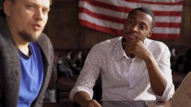 Genç ve yakışıklı afro-amerikan öğrenci veya serbest çalışan öğretmeniyle veya proje sorumlusuyla masaya oturuyor ve konuşmasını dinliyor ve duvarında Amerikan ya da Amerikan bayrağıyla gülümsüyor..