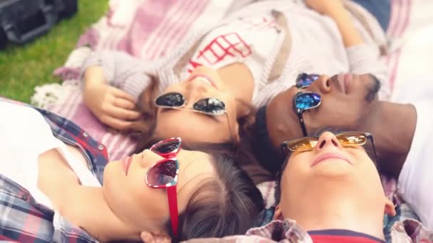 Een groep studenten van verschillende rassen liggen op het gras van top tot teen en lachen. — Stockvideo