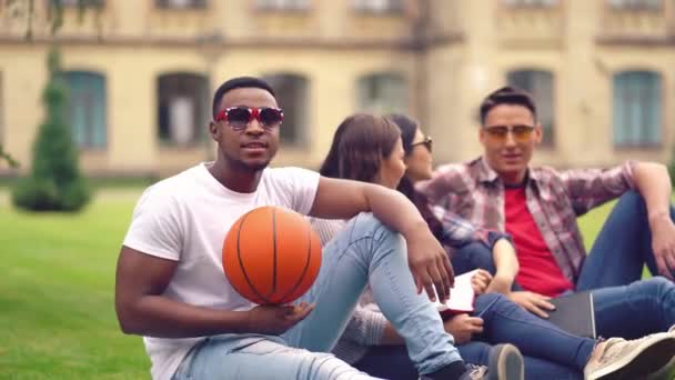 Estudante afro-americano olhando para a câmera enquanto segura uma bola de basquete e sorri — Vídeo de Stock