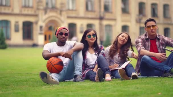 Mutlu öğrenci üniversitenin yakınındaki çimlerde oturarak vakit geçiriyor. — Stok video