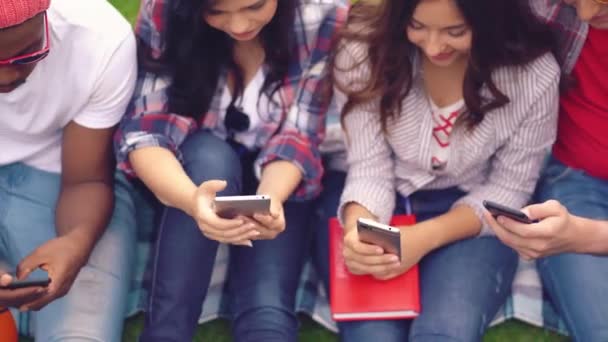 Jovens estudantes de diferentes raças sentam-se escolhendo smartphones — Vídeo de Stock