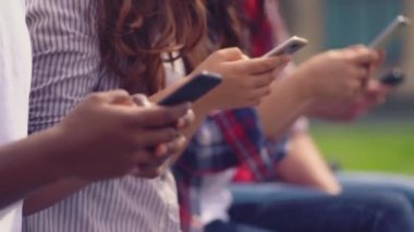 Üniversite öğrencileri çimenlerde oturmuş akıllı telefonlara bakıyor ya da oyun oynuyorlar..