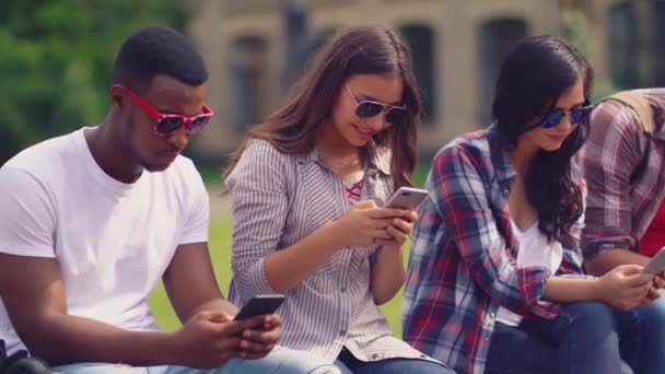 Группа улыбающихся друзей смотрит на мобильные телефоны на улице — стоковое видео