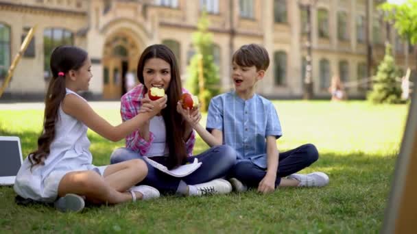 Хлопчик і дівчинка діляться своїми яблуками з матір'ю-фрілансеркою, яка сидить надворі. — стокове відео