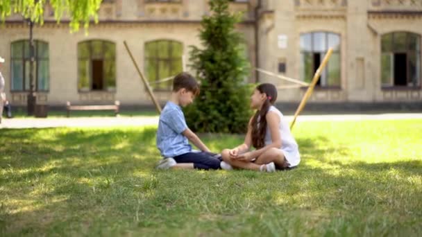 Ung pojke och en flicka sitter på gräset och pratar. — Stockvideo