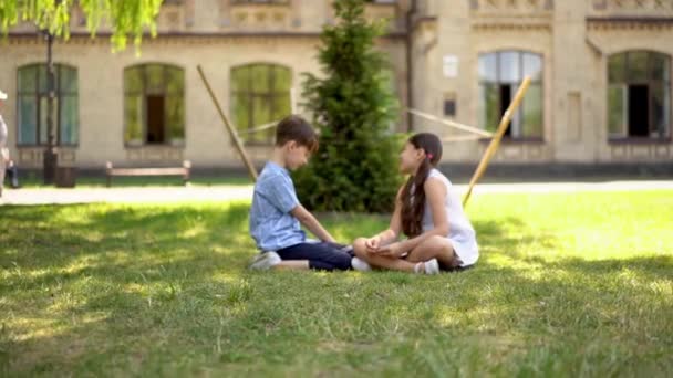 Young boy and a girl sitting on the grass and talking. — Stock Video